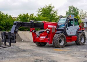 Roter Manitou Teleskoplader auf Baustelle mit Bäumen im Hintergrund.