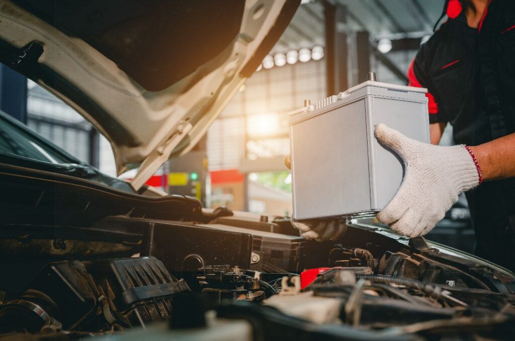Ein Kfz-Mechaniker in einer Werkstatt holt eine neue Batterie ab, um sie im Fahrzeug einzubauen. Für Fahrzeuge, bei denen der Service „Batteriewechsel in der Werkstatt“ in Anspruch genommen wird.